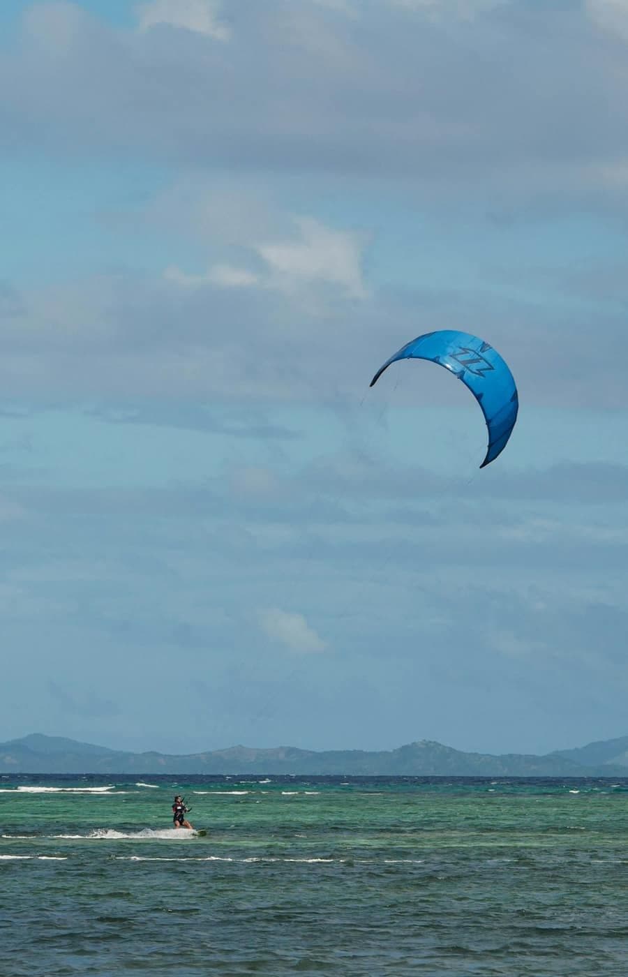 A kitesurfer rides turquoise water beneath a large blue kite.